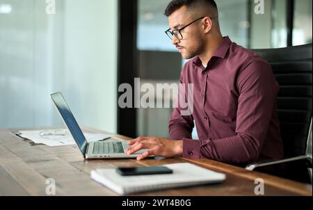 Geschäftiger, junger Geschäftsmann aus Lateinamerika, der am Laptop arbeitet und am Schreibtisch sitzt. Stockfoto