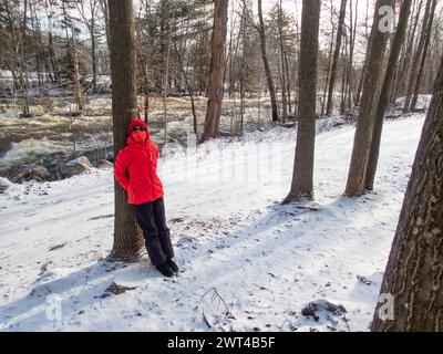 Während der COVID-Epidemie stand eine Frau mit Maske im Park im Winter neben West River, Brownsburg-Chatham, Quebec, Kanada, Stockfoto