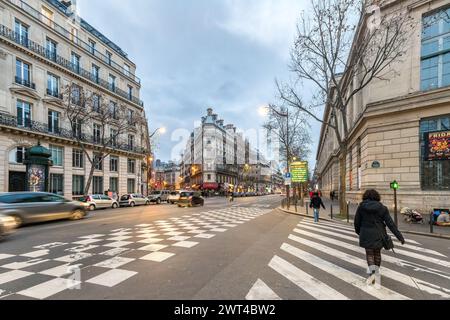 Fußgänger überqueren in der Dämmerung die belebten Straßen von Paris mit klassischer Architektur am Boulevard. Stockfoto