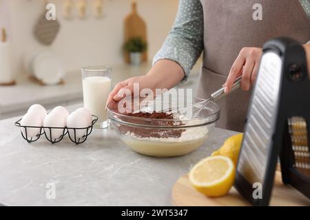 Frau macht Schokoladenteig mit Schneebesen in Schüssel an grauem Marmortisch, Nahaufnahme Stockfoto