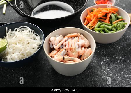 Garnelen, Gemüse und Nudeln zum Kochen von Wok auf grauem, strukturiertem Tisch, Nahaufnahme Stockfoto