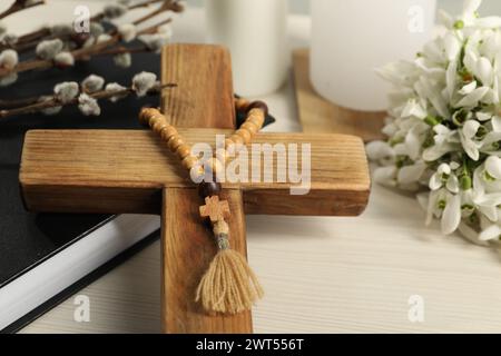 Holzkreuz, Rosenkranzperlen, Bibel, Weidenzweige und Schneeglöckchen auf weißem Tisch, Nahaufnahme Stockfoto