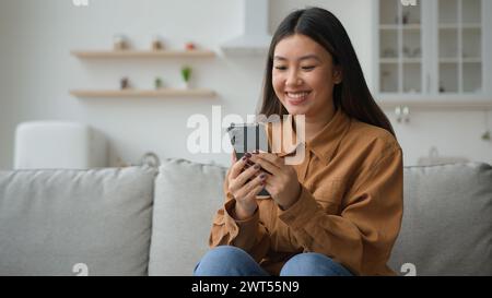 Asiatisch chinesisch koreanisch Geschäftsfrau Frau Mädchen Freiberufler Arbeit von zu Hause in der Küche lesen gute Nachrichten lächelnd Handy benutzen Waren im Internet wählen Stockfoto