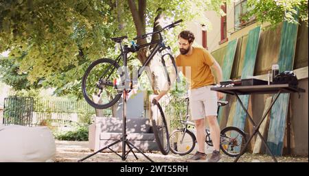 Sportlich engagierter Mann, der beschädigte Fahrräder mit spezieller Ausrüstung aus Werkzeugkasten im Hof repariert. Gesunde kaukasische männliche Demontage Rad und Wartung Fahrrad Vordergabel. Rückziehbild. Stockfoto