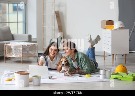 Ein junges Paar mit Beagle-Hund, der während der Reparatur in ihrem neuen Haus einen Laptop auf dem Boden benutzt Stockfoto