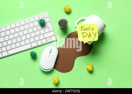 Computertastatur, Haftnotiz und Streich mit verschütteter Tasse Kaffee auf grünem Hintergrund. April-Narrentag-Streich Stockfoto