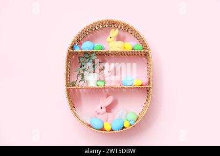 Korbregal mit Osterdekorationen, die an der pinken Wand hängen Stockfoto
