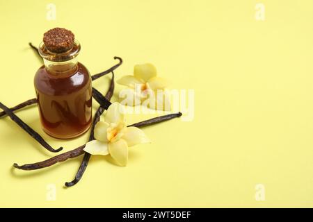 Vanilleextrakt in Flasche mit Vanilleschoten und Blüten auf gelbem Hintergrund Stockfoto