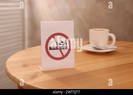 Rauchverbotsschild und eine Tasse Drink auf dem Holztisch drinnen, selektiver Fokus Stockfoto