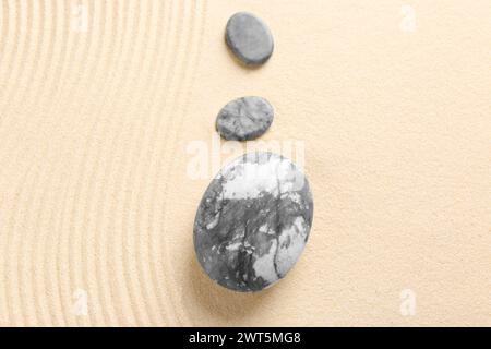 Zen-Gartensteine auf beigem Sand mit Muster, flach angelegt Stockfoto