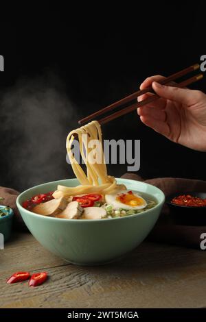 Frau isst köstliche Ramen mit Stäbchen am Holztisch, Nahaufnahme. Nudelsuppe Stockfoto