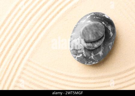 Zen-Gartensteine auf beigem Sand mit Muster, Blick von oben. Leerzeichen für Text Stockfoto