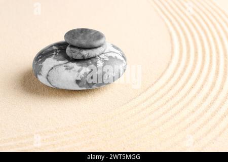 Zen-Gartensteine auf beigem Sand mit Muster. Leerzeichen für Text Stockfoto