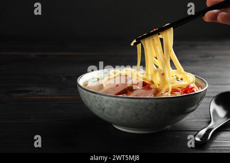 Frau isst köstliche Ramen mit Stäbchen an schwarzem Holztisch, Nahaufnahme und Platz für Text. Nudelsuppe Stockfoto