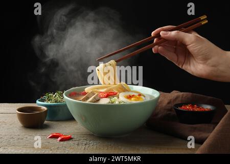 Frau isst köstliche Ramen mit Stäbchen am Holztisch, Nahaufnahme. Nudelsuppe Stockfoto