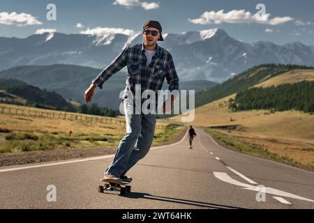 Glückliche Erwachsene Skateboarder fahren auf Longboard auf der geraden Bergstraße Stockfoto