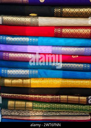 Ordentlich gestapelte farbenfrohe Designer-Seidensaris in Regalen in einem Textilgeschäft. Unglaubliches Indien. Stockfoto