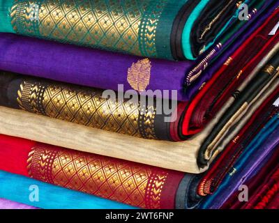 Ordentlich gestapelte farbenfrohe Designer-Seidensaris in Regalen in einem Textilgeschäft. Unglaubliches Indien. Stockfoto