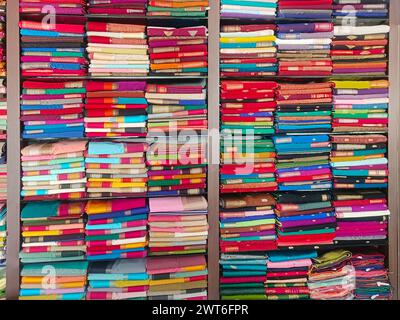 Ordentlich gestapelte farbenfrohe Designer-Seidensaris in Regalen in einem Textilgeschäft. Unglaubliches Indien. Stockfoto