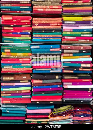 Ordentlich gestapelte farbenfrohe Designer-Seidensaris in Regalen in einem Textilgeschäft. Unglaubliches Indien. Stockfoto