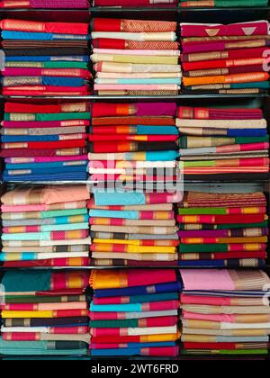 Ordentlich gestapelte farbenfrohe Designer-Seidensaris in Regalen in einem Textilgeschäft. Unglaubliches Indien. Stockfoto