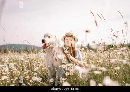 Mädchenhund Wiesen-Kamille. Ein Kind begrüßt ihren pelzigen Freund Maremma Sheepdog in einem ruhigen Kamillenfeld, umgeben von üppigem Grün. Liebe und Stockfoto