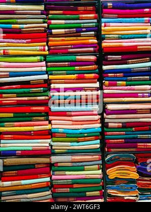 Ordentlich gestapelte farbenfrohe Designer-Seidensaris in Regalen in einem Textilgeschäft. Unglaubliches Indien. Stockfoto