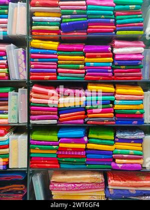 Ordentlich gestapelte farbenfrohe Designer-Seidensaris in Regalen in einem Textilgeschäft. Unglaubliches Indien. Stockfoto
