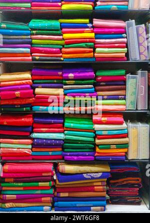 Ordentlich gestapelte farbenfrohe Designer-Seidensaris in Regalen in einem Textilgeschäft. Unglaubliches Indien. Stockfoto