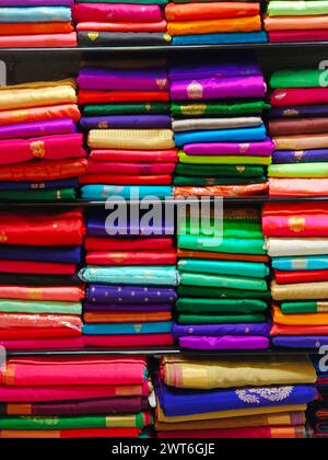 Ordentlich gestapelte farbenfrohe Designer-Seidensaris in Regalen in einem Textilgeschäft. Unglaubliches Indien. Stockfoto