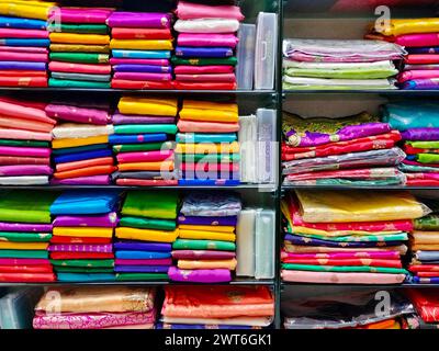Ordentlich gestapelte farbenfrohe Designer-Seidensaris in Regalen in einem Textilgeschäft. Unglaubliches Indien. Stockfoto