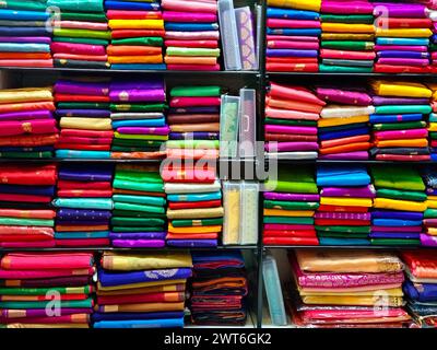 Ordentlich gestapelte farbenfrohe Designer-Seidensaris in Regalen in einem Textilgeschäft. Unglaubliches Indien. Stockfoto