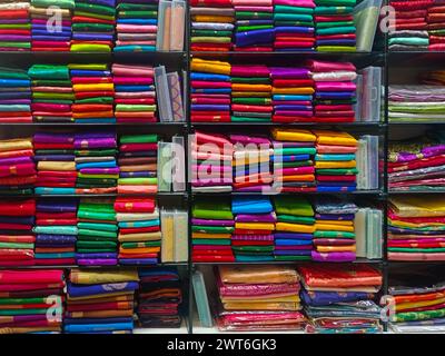 Ordentlich gestapelte farbenfrohe Designer-Seidensaris in Regalen in einem Textilgeschäft. Unglaubliches Indien. Stockfoto