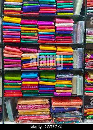 Ordentlich gestapelte farbenfrohe Designer-Seidensaris in Regalen in einem Textilgeschäft. Unglaubliches Indien. Stockfoto