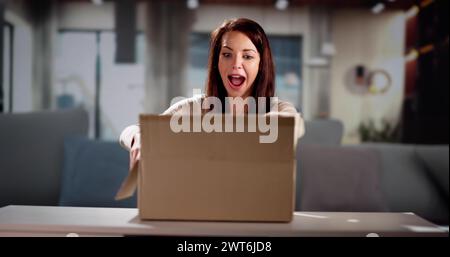 Lächelnde junge Frau sitzt auf einem Sofa Auspacken empfangene Paket Stockfoto