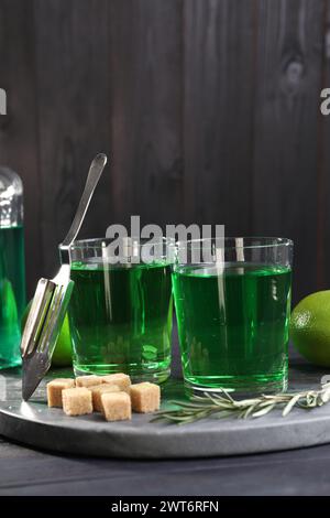 Absinth in Gläsern, Rosmarin, brauner Zucker und Löffel auf dem Tisch. Alkoholisches Getränk Stockfoto