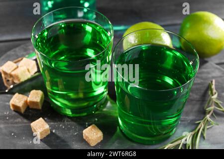 Absinth in Gläsern, Rosmarin, brauner Zucker und Limette auf schwarzem Holztisch, Nahaufnahme. Alkoholisches Getränk Stockfoto