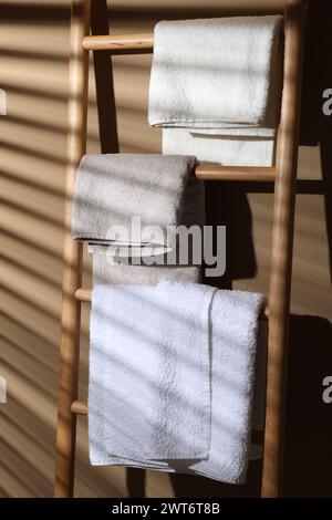Frotteetücher auf einer dekorativen Holzleiter in der Nähe der beigefarbenen Wand Stockfoto