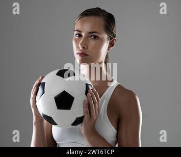 Frau, Porträt und Athletin mit Fußball für Match, Spiel oder Kick-off auf grauem Studiohintergrund. Weibliche Person oder Fußballspieler bereit für Stockfoto