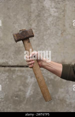 Mann mit Vorschlaghammer nahe der grauen Wand, Nahaufnahme Stockfoto