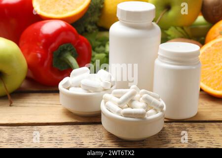 Nahrungsergänzungsmittel. Plastikflaschen, Pillen in Schüsseln und Lebensmittel auf Holztisch Stockfoto