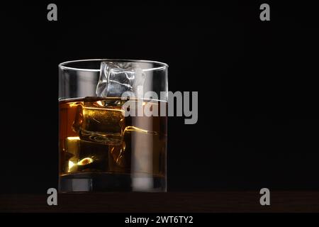 Whiskey mit Eiswürfeln in Glas auf Tisch vor schwarzem Hintergrund. Leerzeichen für Text Stockfoto