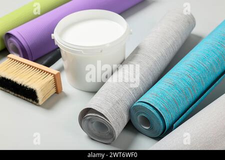 Verschiedene Tapetenrollen, Pinsel und Eimer mit Klebstoff auf hellem Hintergrund Stockfoto
