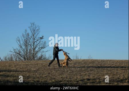 Mann spielt mit seinem Hund auf einem Feld an einem Wintertag, blauer Himmel Hintergrund Stockfoto