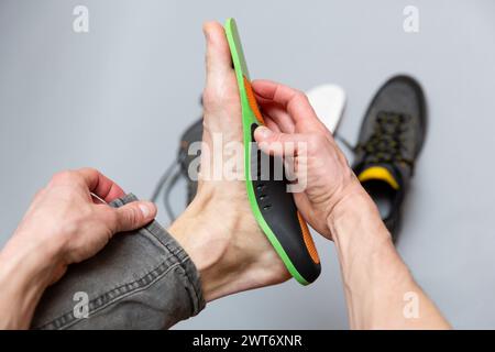 Nahaufnahme von Menschenhänden, die orthopädische Einlagen auf grauem Hintergrund passen. Medizinische und orthopädische Behandlung und Prävention von Plattfüßen Konzept. Stockfoto