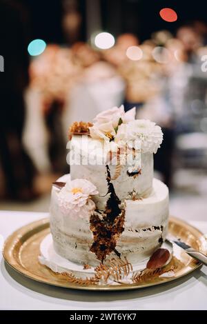 Zweistöckige Hochzeitstorte mit Blumen und ausgeschnittenem Sektor steht auf einem Tablett auf dem Tisch Stockfoto