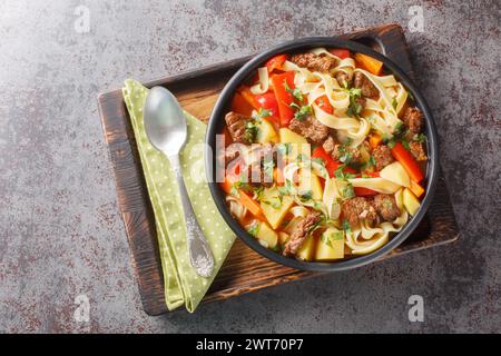 Laghman handgezogene Nudeln in Tomaten- und Lammeintopf aus der Nähe auf dem Teller auf dem Holzbrett. Horizontale Draufsicht von oben Stockfoto