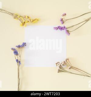 Kreatives Layout aus bunten trockenen Blumen mit Papierkartennotiz auf pastellfarbenem cremefarbenen Hintergrund. Grußkarte mit Blumenmuster. Minimales Konzept und Einfachheit. Stockfoto