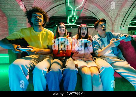 Multiethnische Gruppe junger Freunde, die zu Hause Videospiele spielen und auf dem Sofa sitzen - Videospieler, die Spaß beim E-Sport haben, während Computervideospiel-Nachteile spielen Stockfoto