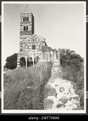 Sardinien Sassari Sassari (Environs) SS. Trinita di Saccargia (Camaldolite). Hutzel, Max 1960-1990 Außenansichten einer romanischen Kirche (12. Jahrhundert) umfassen: Eine gestreifte Fassade (dunkler Basalt und weißer Kalkstein), einen Turm mit pisanischem und lucchesischem Einfluss und verzierte/groteske Kapitelle. Antiquitäten: Zwei Säulen und Kapitelle des Portikus. Objektnotizen: Hutzel Fotokampagne Datum: 16. April 1983 der in Deutschland geborene Fotograf und Gelehrte Max Hutzel (1911–1988) fotografierte in Italien von den frühen 1960er Jahren bis zu seinem Tod. Das Ergebnis dieses Projekts, von Hutzel als Foto Arte Minore bezeichnet, ist Thorou Stockfoto